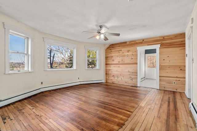 spare room featuring wood-type flooring, baseboard heating, wood walls, and a ceiling fan