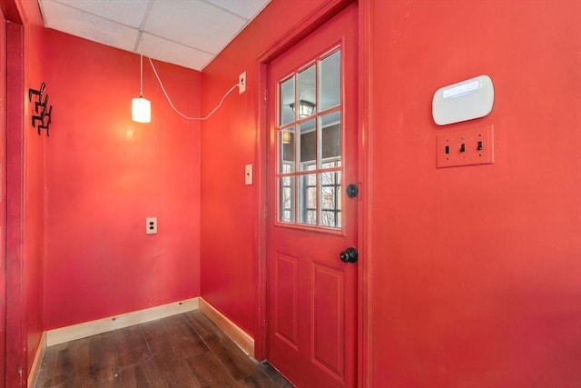 doorway to outside featuring a drop ceiling, baseboards, and dark wood-type flooring