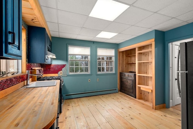 kitchen featuring butcher block countertops, light wood-style flooring, freestanding refrigerator, a baseboard radiator, and a paneled ceiling