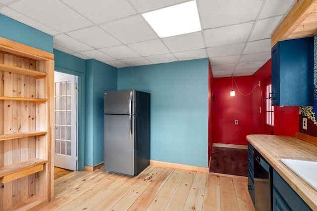 kitchen featuring blue cabinetry, freestanding refrigerator, light wood-style floors, a paneled ceiling, and dishwasher