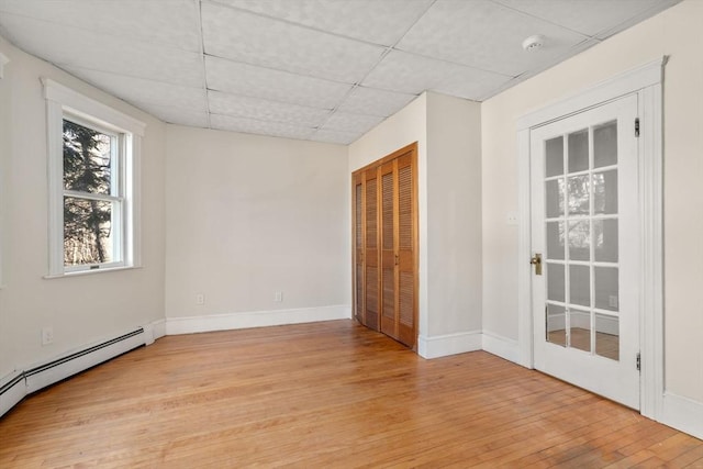 unfurnished room with a baseboard heating unit, a paneled ceiling, light wood-type flooring, and baseboards