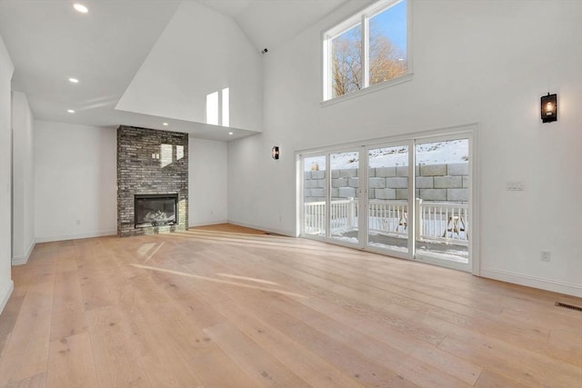 unfurnished living room with a towering ceiling, a brick fireplace, and light hardwood / wood-style flooring