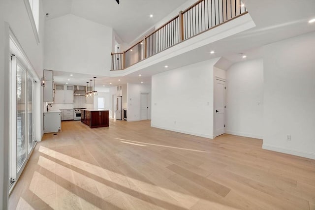 unfurnished living room with light hardwood / wood-style floors, a towering ceiling, and sink