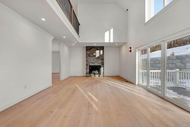 unfurnished living room with light wood-type flooring, a towering ceiling, and a fireplace