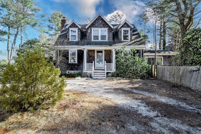 shingle-style home featuring a porch, a chimney, and fence