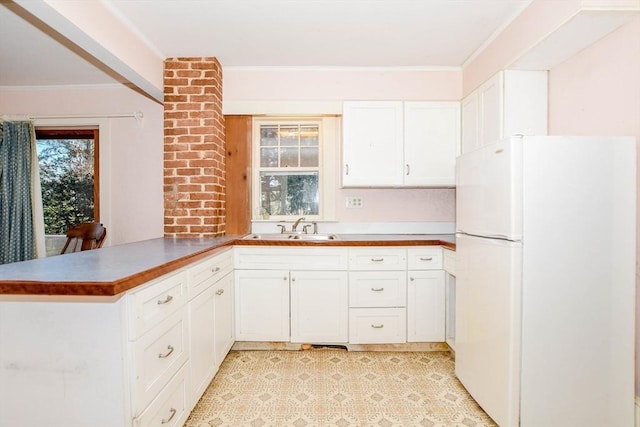 kitchen with ornamental molding, freestanding refrigerator, a peninsula, white cabinetry, and a sink