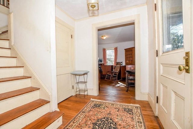 entrance foyer with light wood-style floors, baseboards, stairway, and crown molding