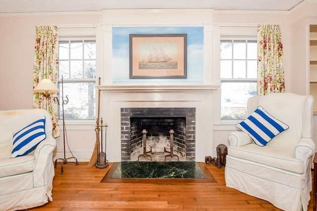 living area with a fireplace with flush hearth, crown molding, and wood finished floors