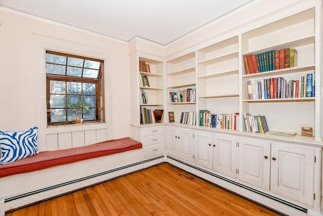 living area featuring light wood-style floors, built in shelves, a baseboard heating unit, and crown molding