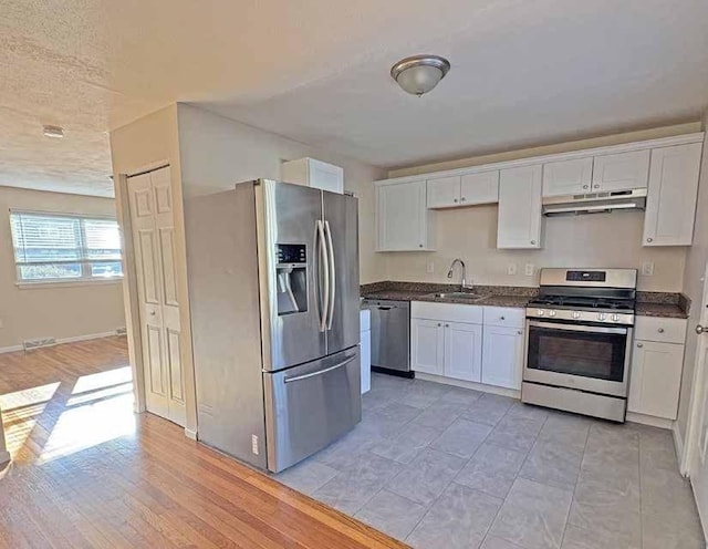 kitchen with appliances with stainless steel finishes, dark countertops, a sink, and under cabinet range hood