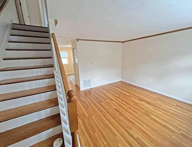 staircase with ornamental molding, visible vents, baseboards, and wood finished floors