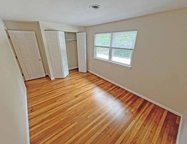 unfurnished bedroom featuring baseboards, a closet, visible vents, and light wood-style floors