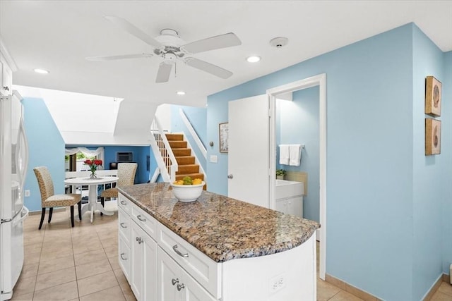 kitchen featuring a center island, light tile patterned flooring, dark stone countertops, white fridge, and white cabinetry