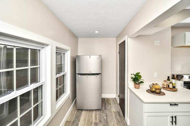 kitchen with stainless steel fridge, white cabinets, and light hardwood / wood-style floors