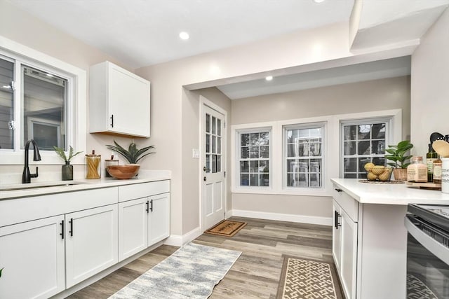 kitchen with black range with electric cooktop, white cabinetry, sink, and light wood-type flooring