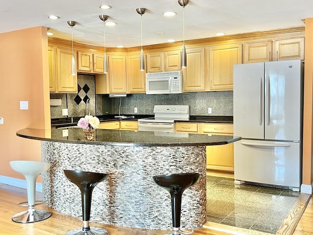 kitchen featuring a kitchen bar, light brown cabinets, hanging light fixtures, and white appliances