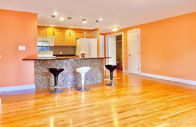 kitchen with decorative light fixtures, backsplash, a breakfast bar, kitchen peninsula, and white appliances