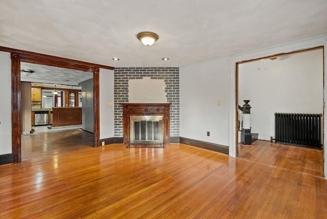 unfurnished living room with baseboards, wood-type flooring, radiator, and a fireplace