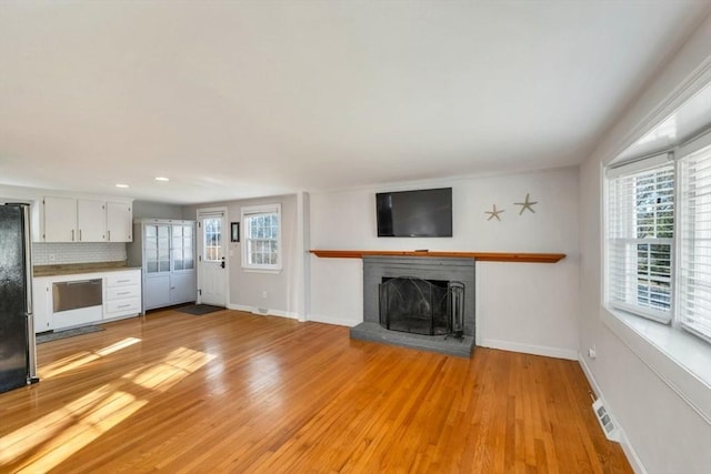 unfurnished living room featuring light hardwood / wood-style flooring, a healthy amount of sunlight, and a brick fireplace