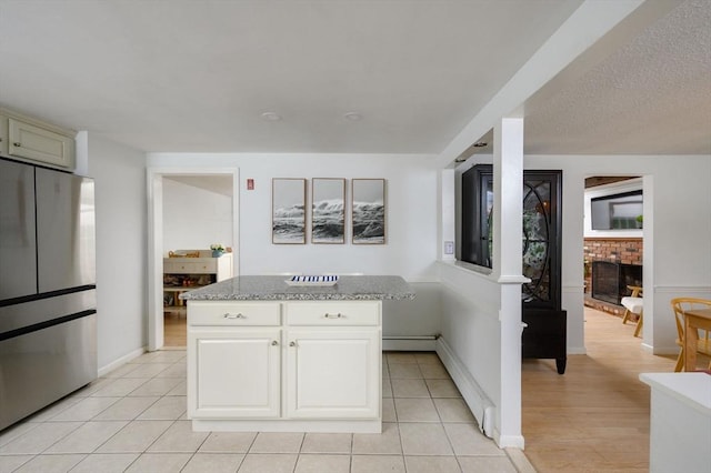 11 Williamsburg Ln, Scituate, MA 02066 - kitchen featuring freestanding refrigerator, a fireplace, a kitchen island, light stone counters, and light tile patterned flooring