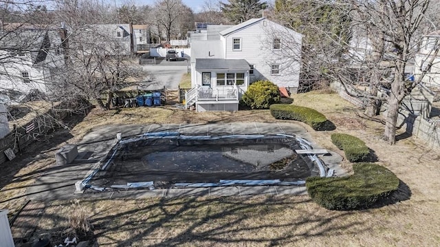 rear view of property featuring a covered pool, a trampoline, and fence