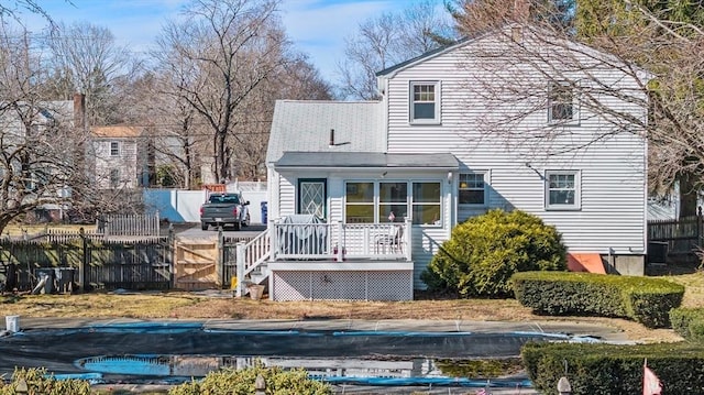 rear view of house with a wooden deck, a covered pool, and fence