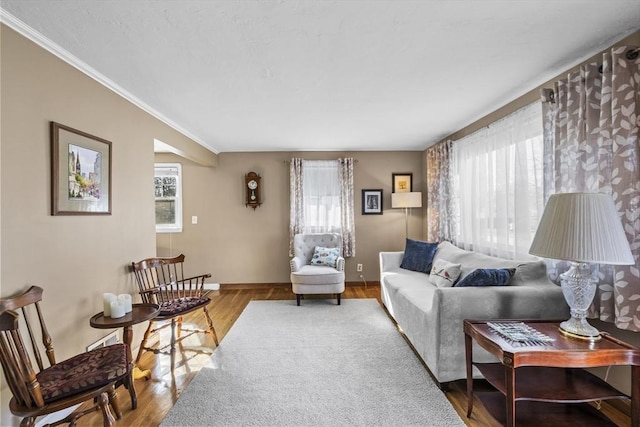 living area with baseboards, a healthy amount of sunlight, wood finished floors, and ornamental molding