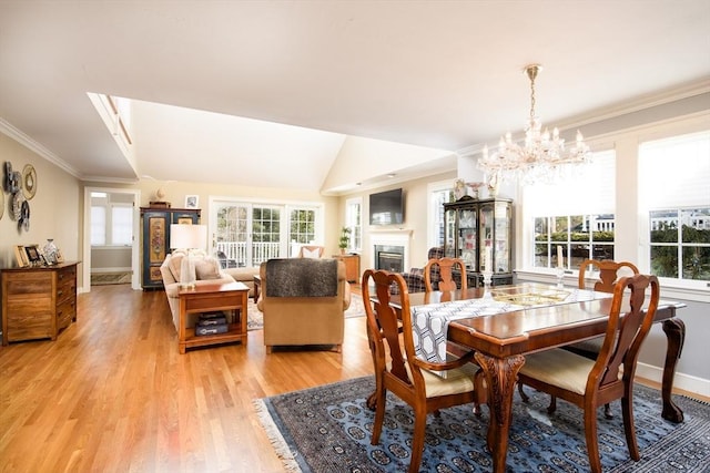 dining space with baseboards, a glass covered fireplace, ornamental molding, an inviting chandelier, and light wood-style floors