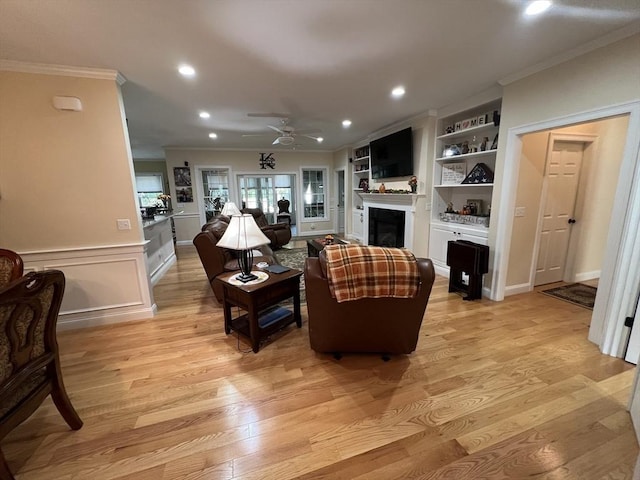 living room featuring ornamental molding, ceiling fan, light wood-type flooring, and built in shelves