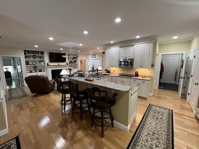 kitchen featuring a large island, light hardwood / wood-style flooring, ornamental molding, light stone countertops, and a kitchen bar