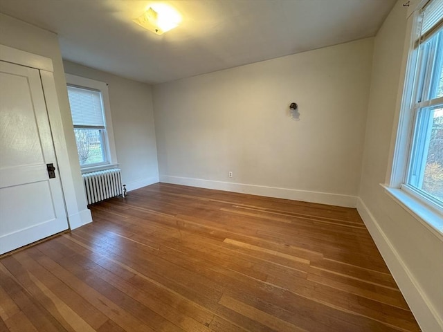 empty room featuring a healthy amount of sunlight, radiator heating unit, and wood-type flooring