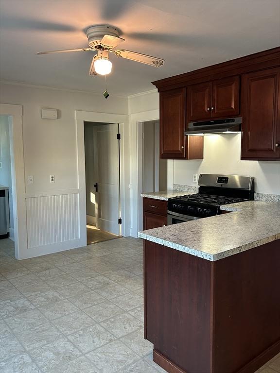 kitchen featuring dark brown cabinetry, ceiling fan, crown molding, and stainless steel gas range