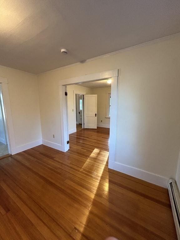 spare room with baseboard heating, crown molding, and wood-type flooring