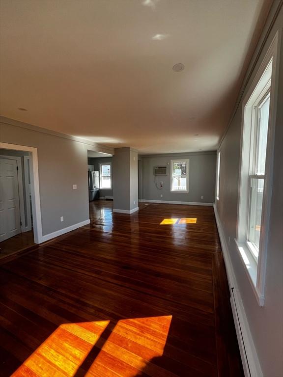 unfurnished living room featuring a wall unit AC, wood finished floors, baseboards, and a wealth of natural light