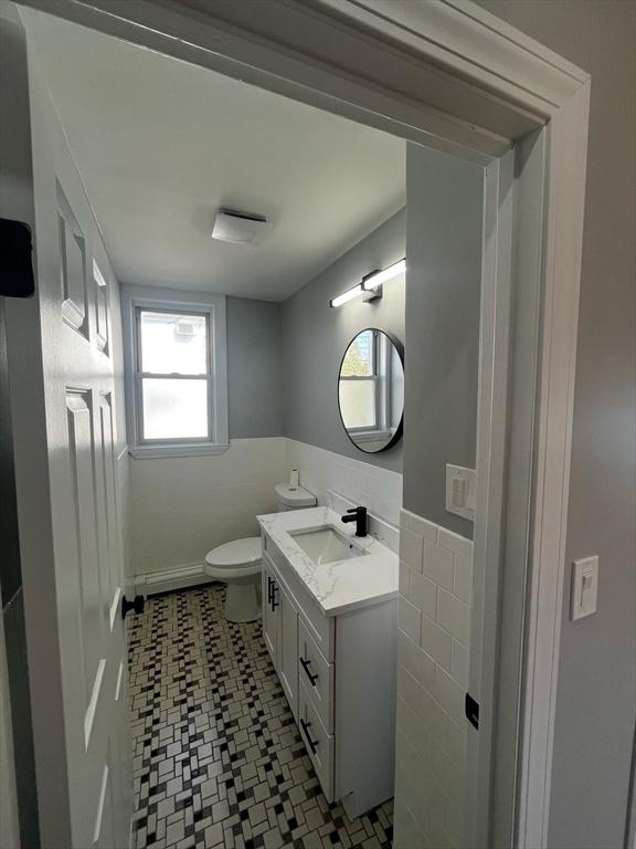 half bath featuring vanity, toilet, a healthy amount of sunlight, and a wainscoted wall