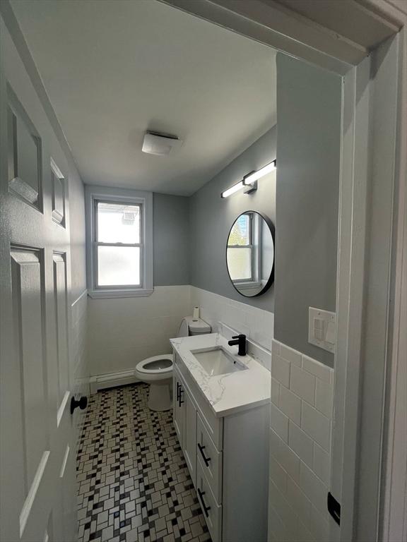 bathroom featuring vanity, a wainscoted wall, a baseboard radiator, tile walls, and toilet