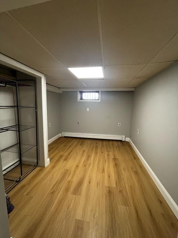 basement with light wood-style flooring, a paneled ceiling, baseboards, and baseboard heating