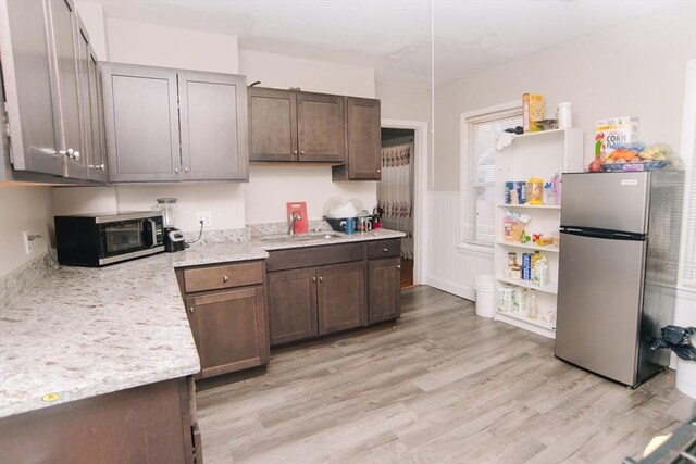 kitchen featuring wainscoting, dark brown cabinets, a sink, light wood-style floors, and stainless steel appliances