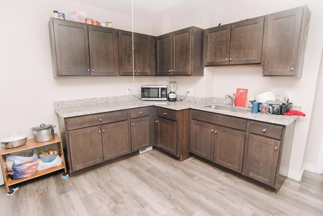 kitchen featuring light wood-style floors, stainless steel microwave, a sink, and dark brown cabinets