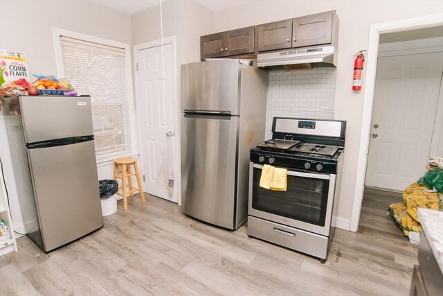 kitchen with backsplash, appliances with stainless steel finishes, dark brown cabinets, under cabinet range hood, and light wood-style flooring