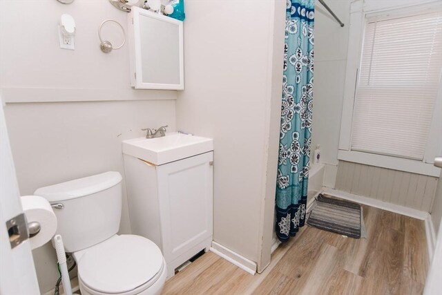 bathroom with vanity, wood finished floors, toilet, baseboards, and shower / bathtub combination with curtain