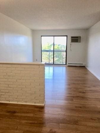 10 Williams St Unit 79, Watertown, MA 02472 - unfurnished room featuring wood finished floors, a wall mounted air conditioner, a baseboard heating unit, and baseboards