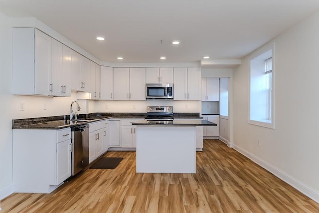 kitchen featuring dark stone countertops, appliances with stainless steel finishes, light wood-type flooring, a kitchen island, and white cabinetry