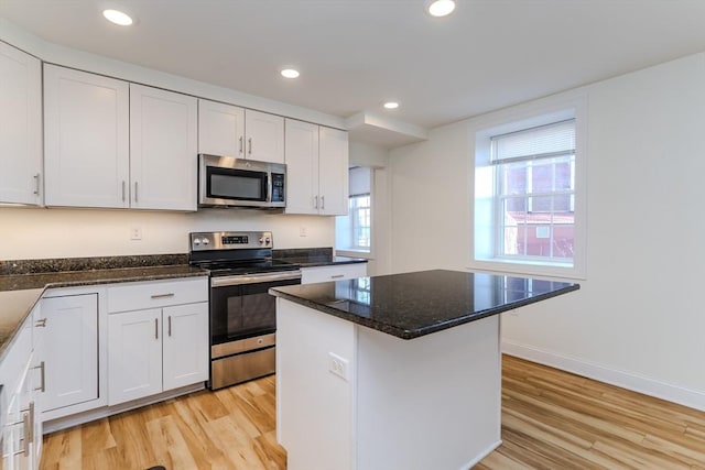 kitchen featuring white cabinetry, dark stone countertops, light hardwood / wood-style flooring, a kitchen island, and appliances with stainless steel finishes