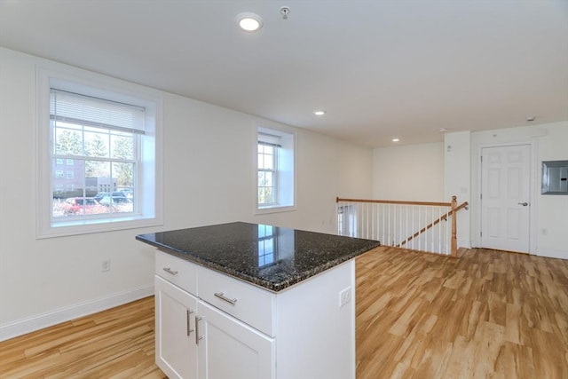 kitchen with a center island, dark stone countertops, light hardwood / wood-style flooring, and white cabinetry