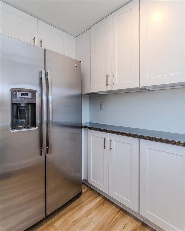 kitchen with stainless steel refrigerator with ice dispenser, white cabinets, dark stone counters, and light hardwood / wood-style flooring