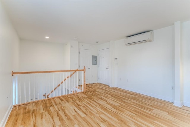 spare room featuring electric panel, light hardwood / wood-style floors, and a wall mounted air conditioner