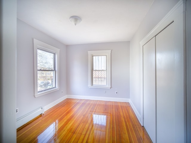 unfurnished bedroom with hardwood / wood-style flooring, a closet, and a baseboard heating unit