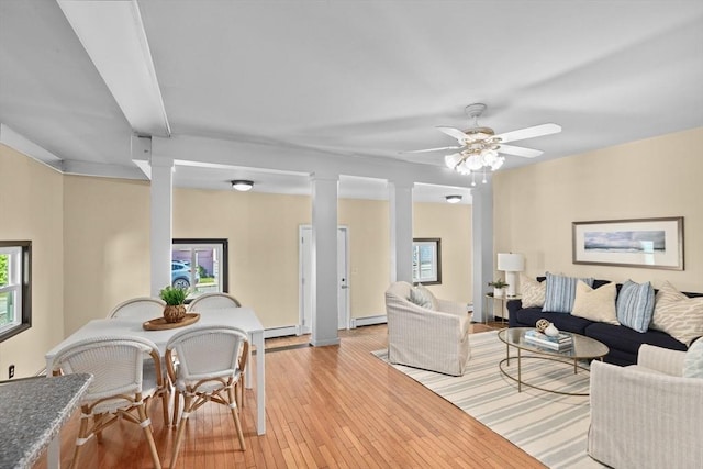 living area with light wood finished floors, a baseboard radiator, a ceiling fan, and ornate columns