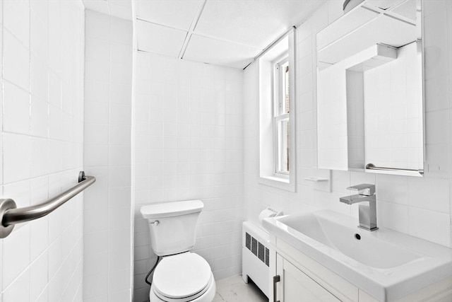 half bathroom with toilet, radiator heating unit, vanity, and tile walls